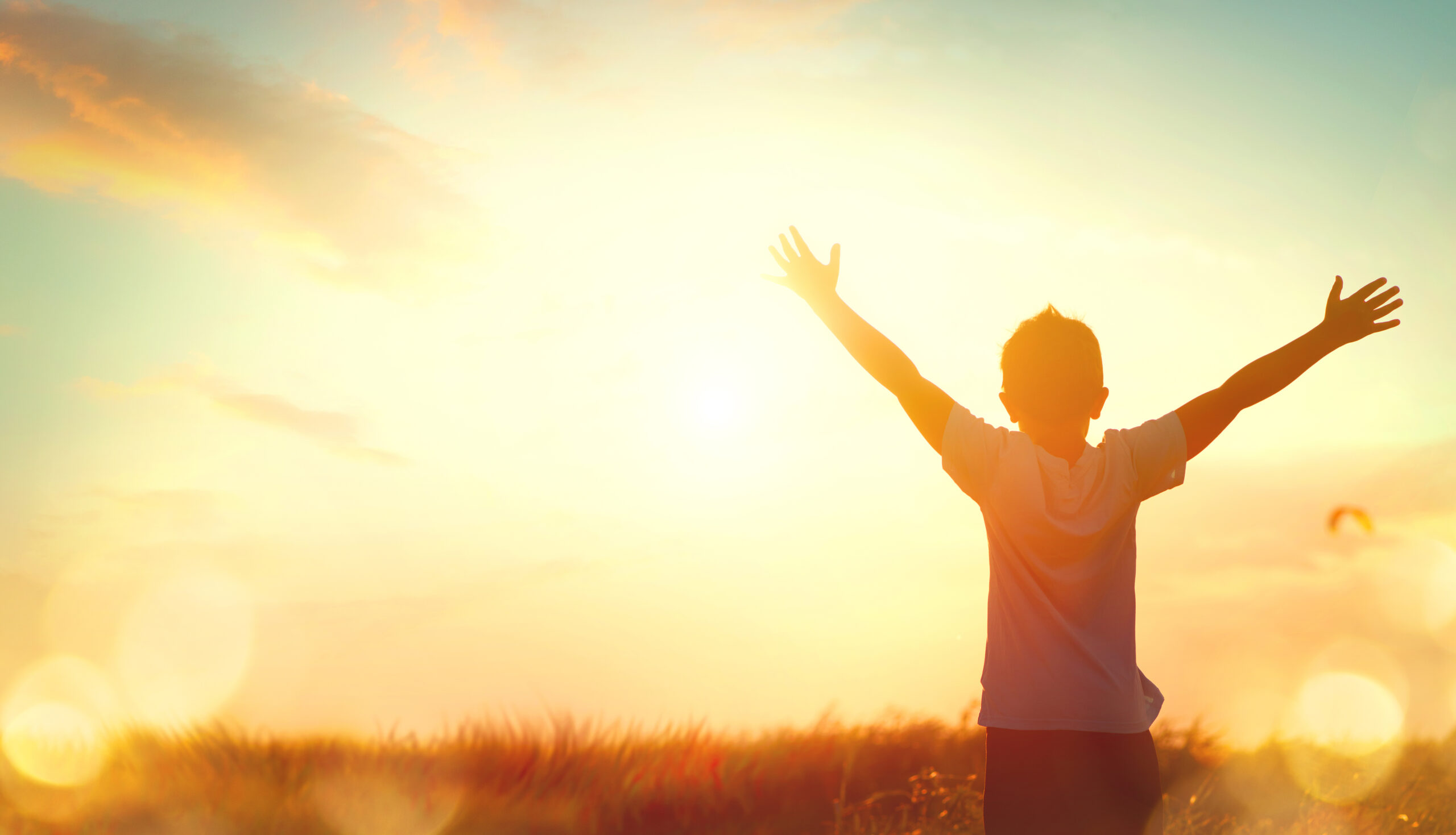 A child with outstretched arms stands in a field at sunrise