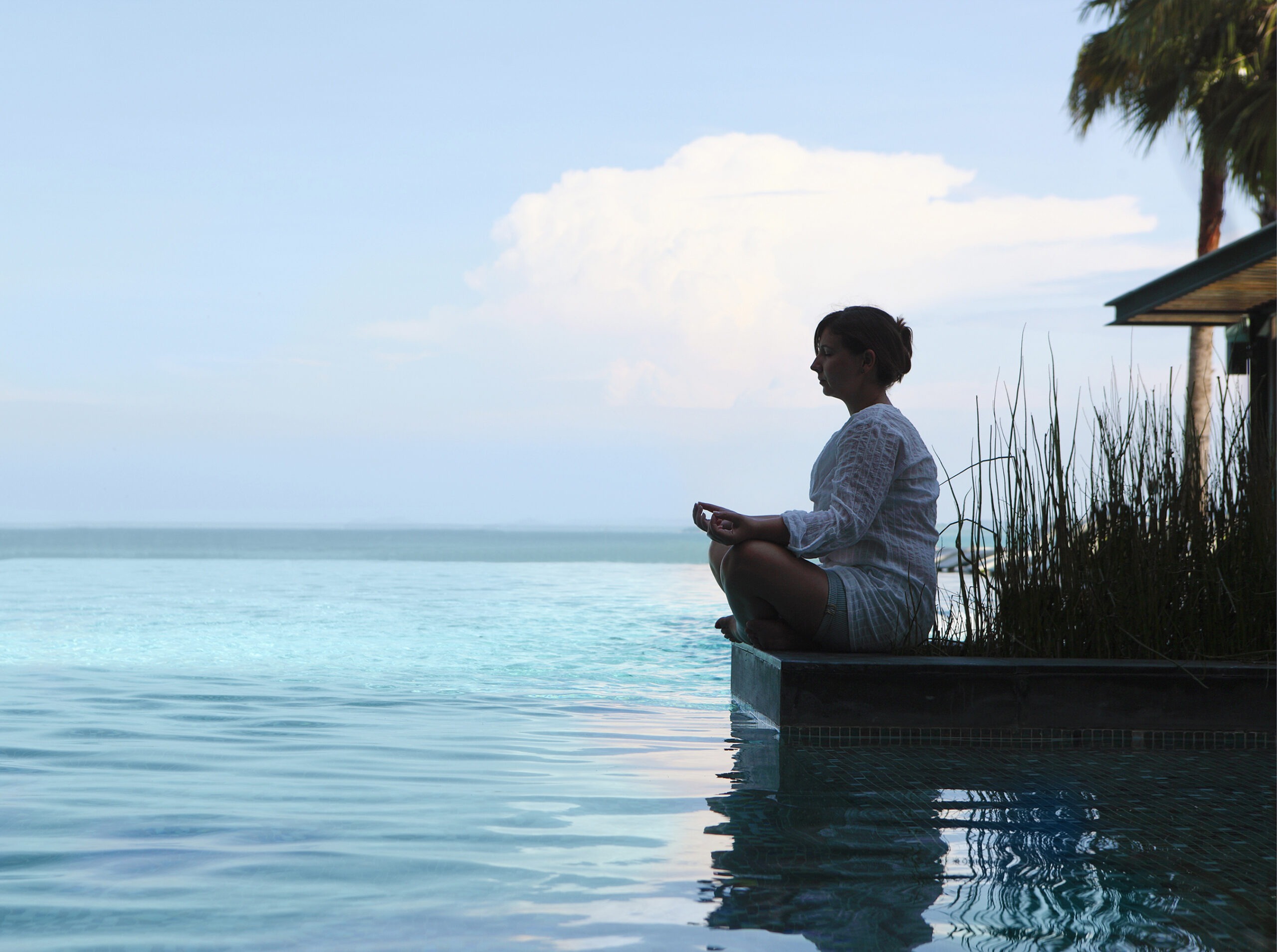 A woman meditates at the edge of a tranquil infinity pool