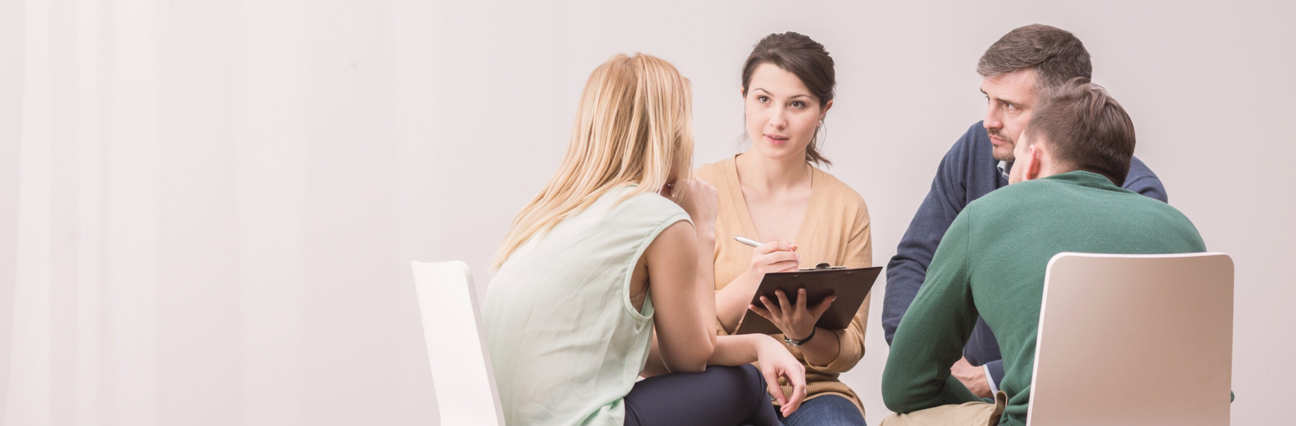 A diverse group of four people engaged in a discussion, with one woman taking notes on a clipboard