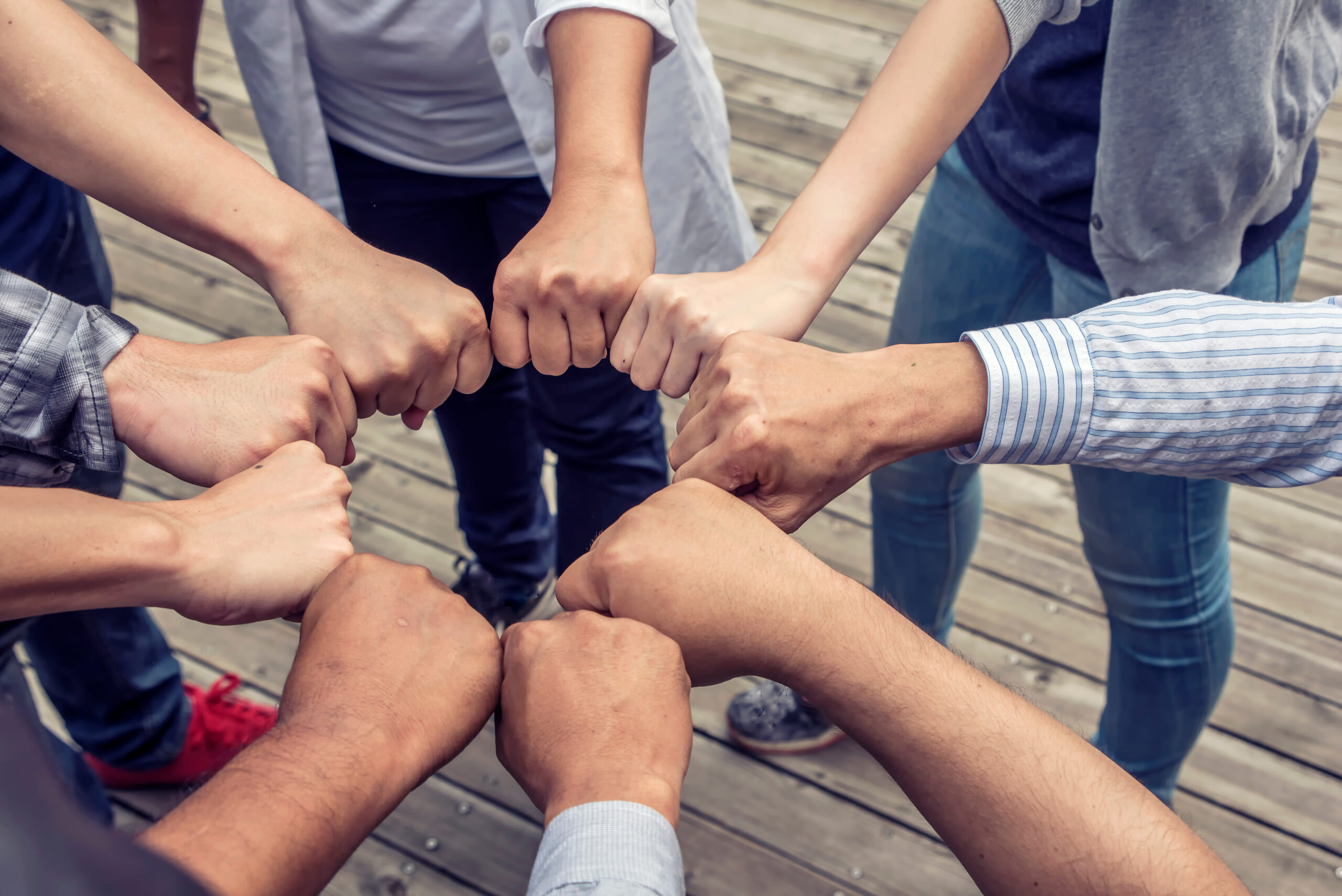 A circle of diverse hands creating a fist bump, symbolizing unity and collaboration, set on a wooden deck.
